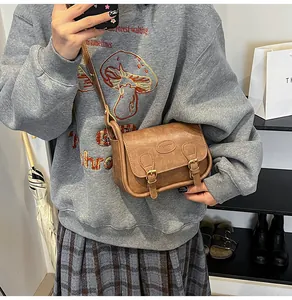 Macro shot of brown vintage PU leather crossbody bag featuring dual buckle details and logo