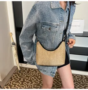 Détail d'un sac en paille style dumpling avec liseré en cuir noir et bandoulière réglable