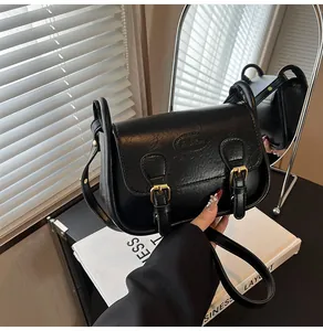 Close-up of black PU leather saddle bag with gold metal buckles and fashion embossed logo