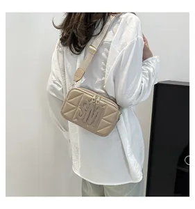 Detail van beige gewatteerde crossbodytas met SM-logo-reliëf en brede stoffen riem