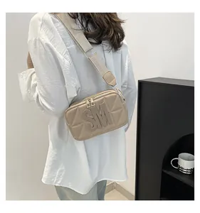 Detail van beige crossbodytas met SM-letterpatch en brede stoffen schouderband