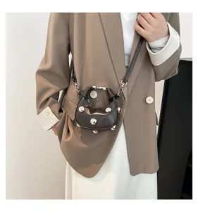 Detail of a dark brown mini crossbody bag with silver studs worn with a beige blazer