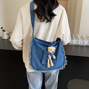 Detailed view of the denim crossbody bag with fringe edges and a cute brown plush bear