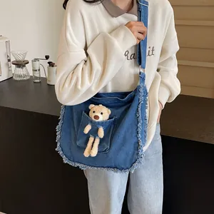 Detail of denim tote bag featuring a plush bear in front pocket and frayed edge trim