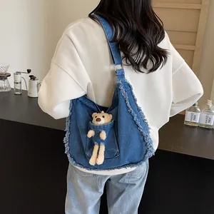 Detail of blue denim tote bag featuring a plush bear in front pocket with frayed edges