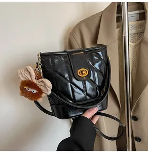 Détail d'un sac seau noir matelassé avec fermoir doré rotatif et un pendentif en peluche