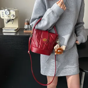 Sac seau matelassé en cuir verni rouge avec fermoir doré et charme en peluche porté