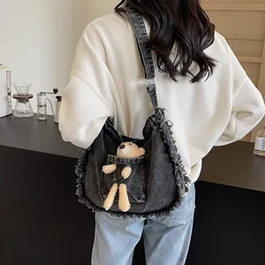 Detail of black denim tote bag with frayed edges and cute plush bear accessory