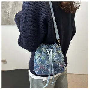 Détail du sac seau en denim bleu avec écussons étoiles colorés et bords effilochés
