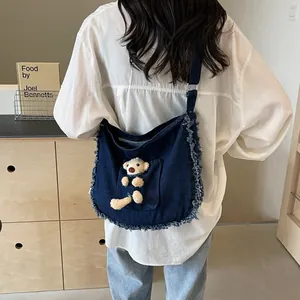 Detail of blue denim tote bag with frayed edges and cute plush bear in the front pocket