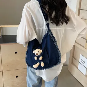Detail of blue denim tote bag with frayed edges and cute plush teddy bear in front pocket