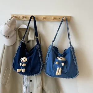 Detail of denim tote bag with plush bear in pocket and frayed edges in blue tones