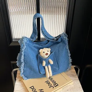 Close-up of denim tote bag featuring fringe details and a cute plush bear accessory