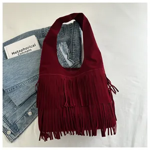 Detail view of deep red suede tote bag with layered tassels on a denim jacket backdrop
