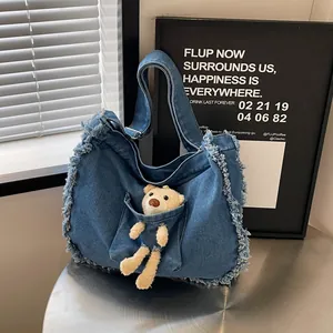 Detail of blue denim tote bag featuring frayed edges and a cute beige plush bear charm
