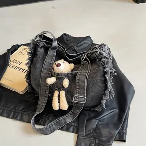 Detail of black washed denim tote bag with raw frayed edges and a cute plush bear charm