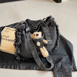 Close-up of black denim tote bag showing frayed fringe edges and mini bear decoration