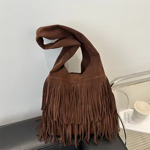 Brown suede tote bag with long fringes and wide strap displayed on a leather chair