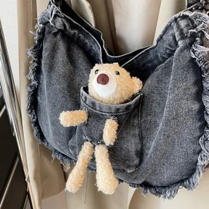Detail of vintage denim tote bag featuring a cute plush bear decoration and frayed edges
