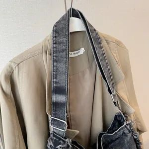 Detailed close-up of a washed denim tote bag with frayed edges and silver metal buckles