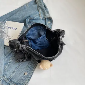 Detail view of denim tote bag showing interior pockets, zipper, and bear charm accessory
