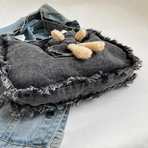 Detailed view of frayed edges and plush decor on a black denim tote shoulder bag