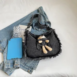 Detailed close-up of a black denim hobo bag with fringe edges and a cute plush bear charm