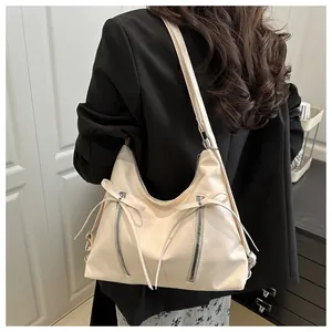 Chic cream PU hobo bag featuring decorative zippers and ribbons worn with black suit