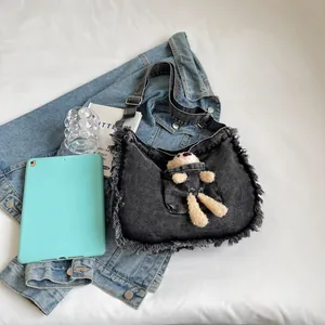 Detail of dark gray denim tote with fringed edges and cute teddy bear in the front pocket