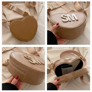 Detail of heart-shaped PU leather bag with silver letters and wide fabric strap