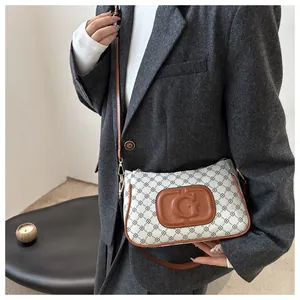 Detail of crossbody bag with beige geometric pattern, brown leather patch, and embossed G