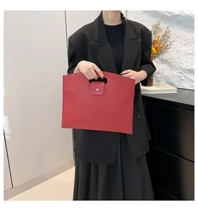 Détail du sac rouge en cuir grainé avec poignée ovale et bouton pression pour bureau