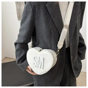 Macro shot of white heart-shaped PU crossbody bag with 3D SM letter detail and wide strap