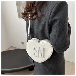 Detail view of a white heart-shaped PU leather crossbody bag with SM embossed letters