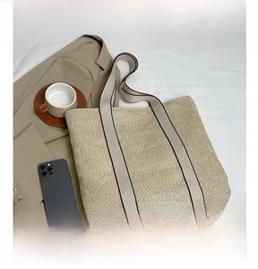 Flat lay of a woven straw tote bag with brown contrast trim on a clean white bedding