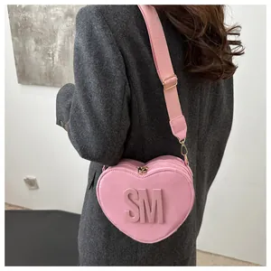 Detail view of pink heart-shaped crossbody bag with embossed SM letters and wide strap
