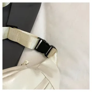 Detail of the quick-release plastic buckle and adjustable nylon strap on the cream chest bag