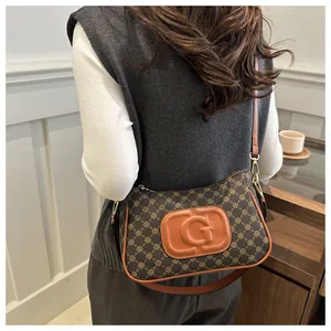 Brown monogram shoulder bag with orange letter G detail worn by model in a minimal setting
