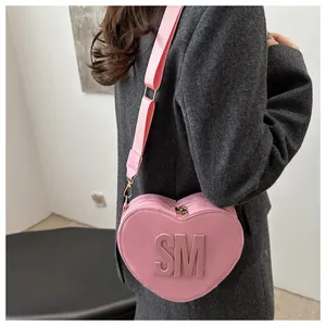 Detail of pink heart-shaped PU crossbody bag with SM logo and wide nylon shoulder strap