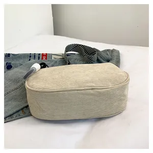 Detail of beige corduroy pillow bag with striped woven strap on a soft white bed