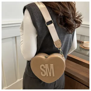 Detail of khaki heart-shaped PU crossbody bag with SM logo and wide woven strap