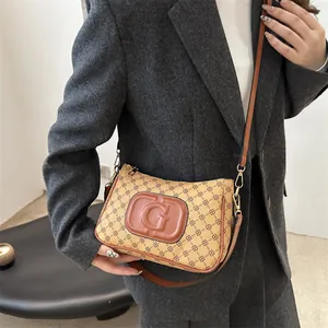 Chic beige monogram crossbody bag with letter G patch worn with a gray blazer