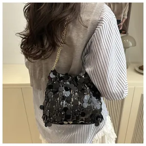 Detail of a black sequin shoulder bag with a gold chain strap worn by a fashion model