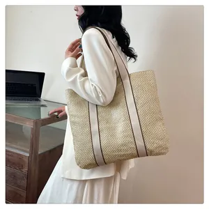 Large woven tote bag with canvas straps shown on shoulder in a minimalist office setting