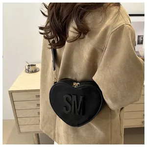 Detail of a black heart-shaped crossbody bag with gold zippers and 3D letters
