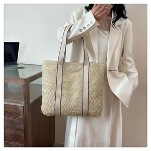 Detail showing the large beige straw tote bag with long handles styled on a model