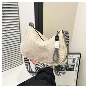 Detail of beige corduroy crescent bag featuring a stylish black and white striped strap