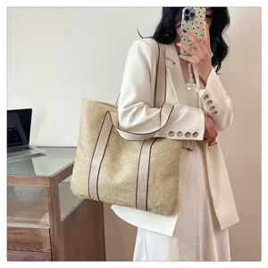 Detail of a large woven straw tote bag featuring beige texture and canvas shoulder straps