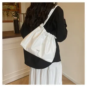 Detail of white pleated drawstring cloud bag with metal bow on model in cafe