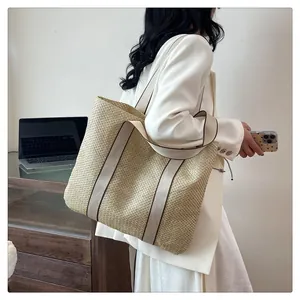 Detail of a large woven straw tote bag with contrast edge canvas straps on a model